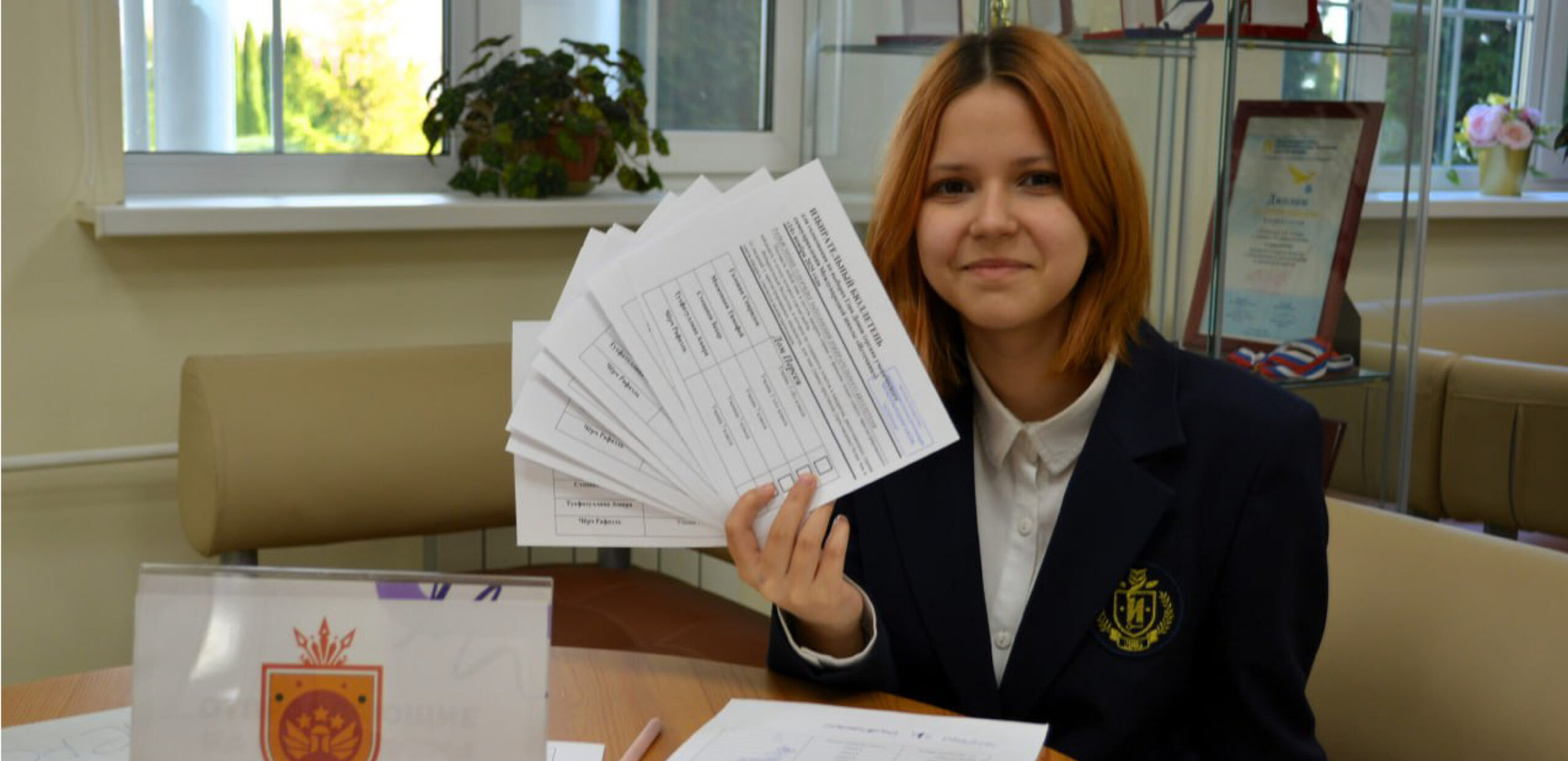 Ученик школы Источник показывает заполненные бюллетени для выборов.