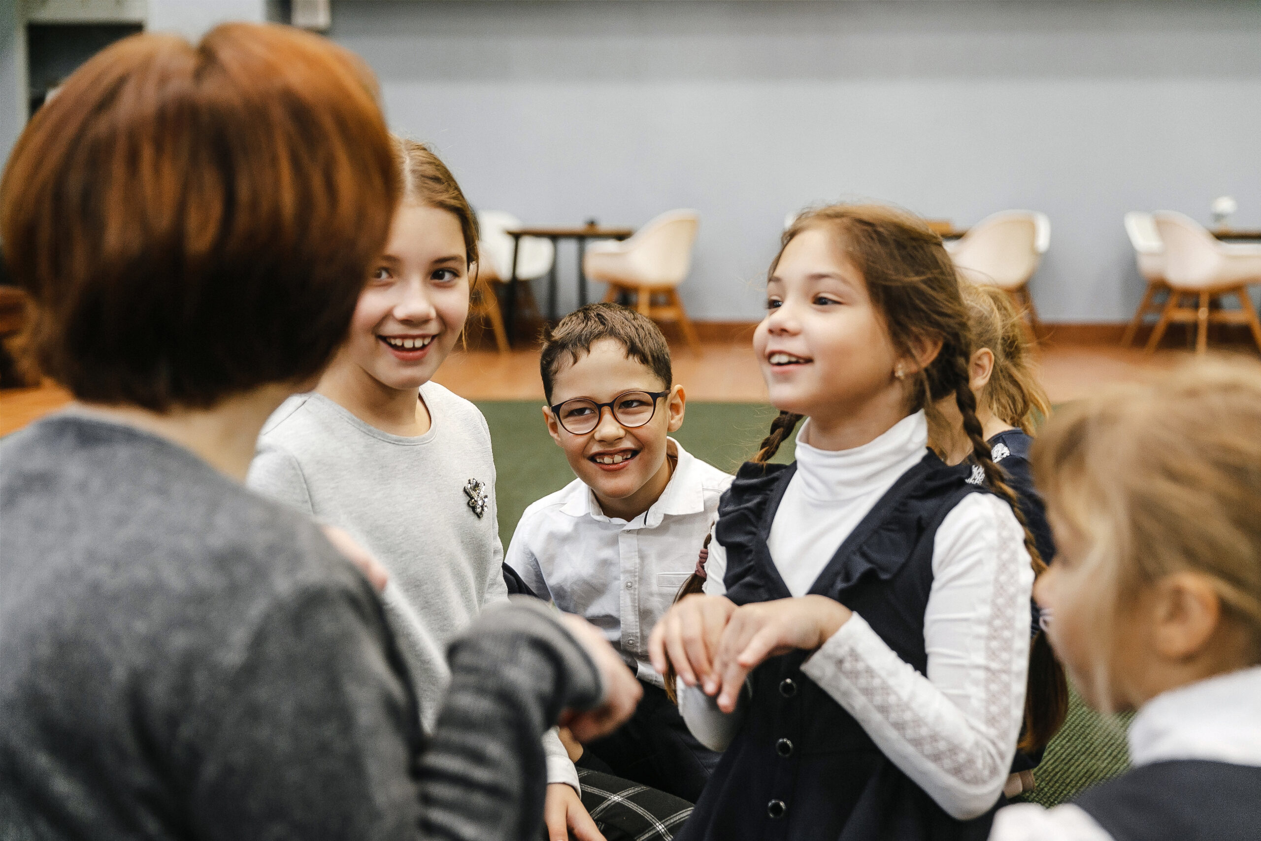 Children smiling and talking with teacher in school common room