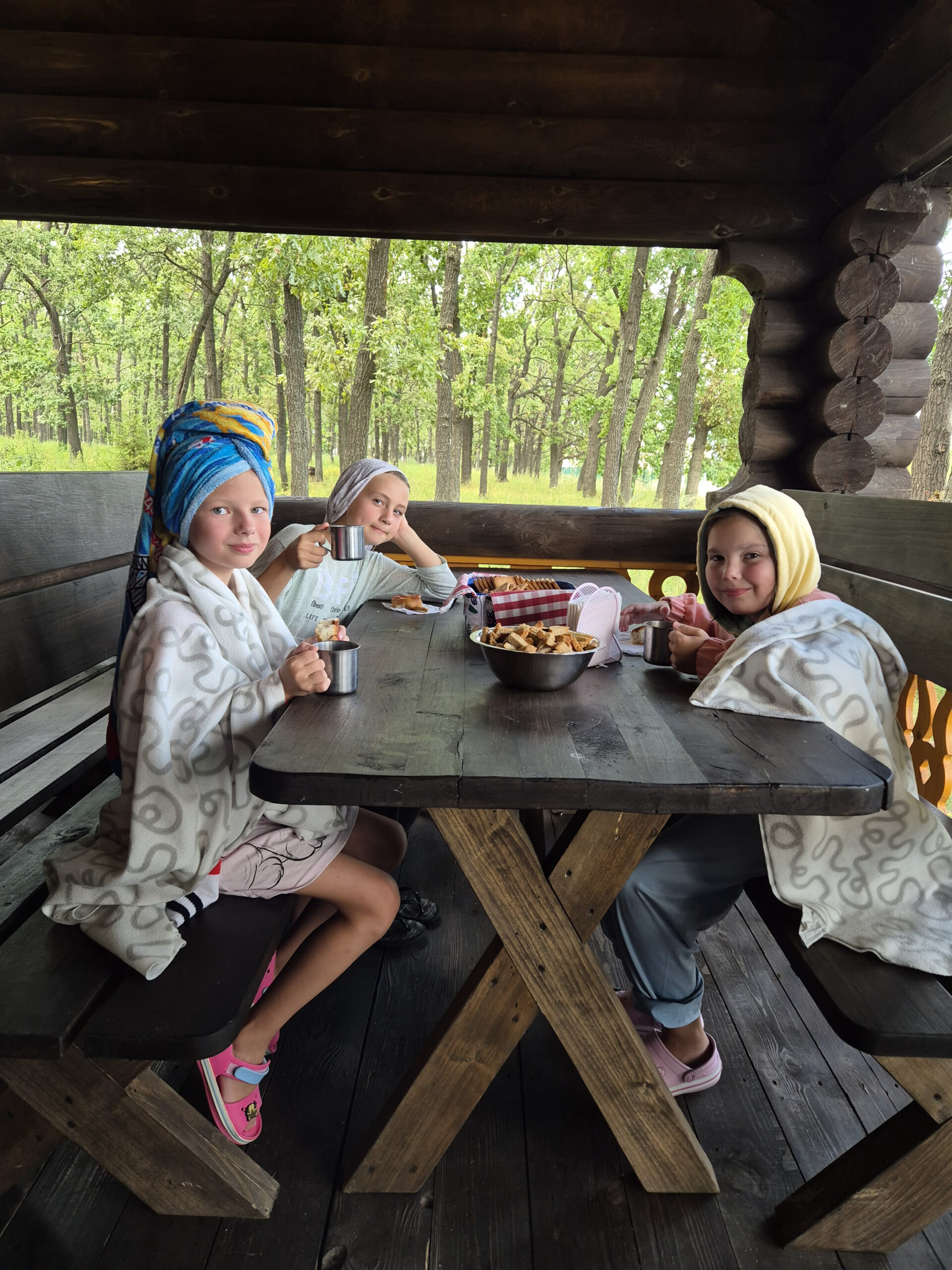 Children in robes drinking tea in a wooden gazebo at the camp in nature