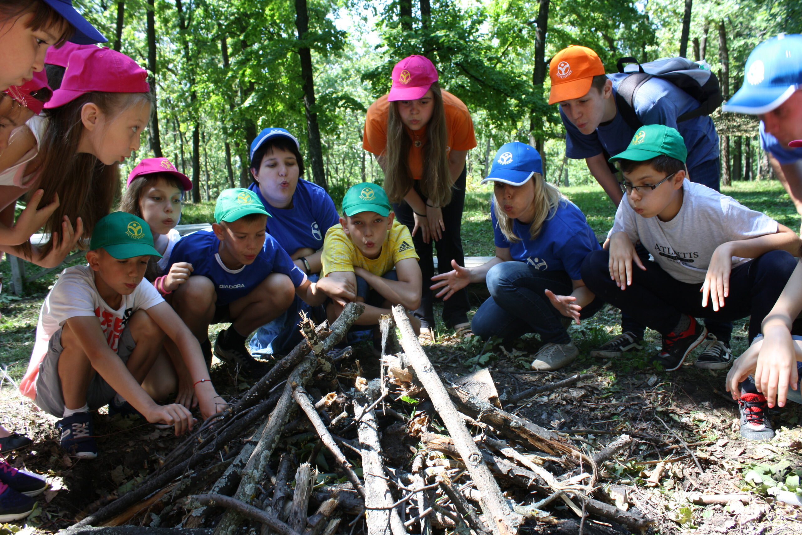Children in colorful caps building a campfire outdoors in the forest