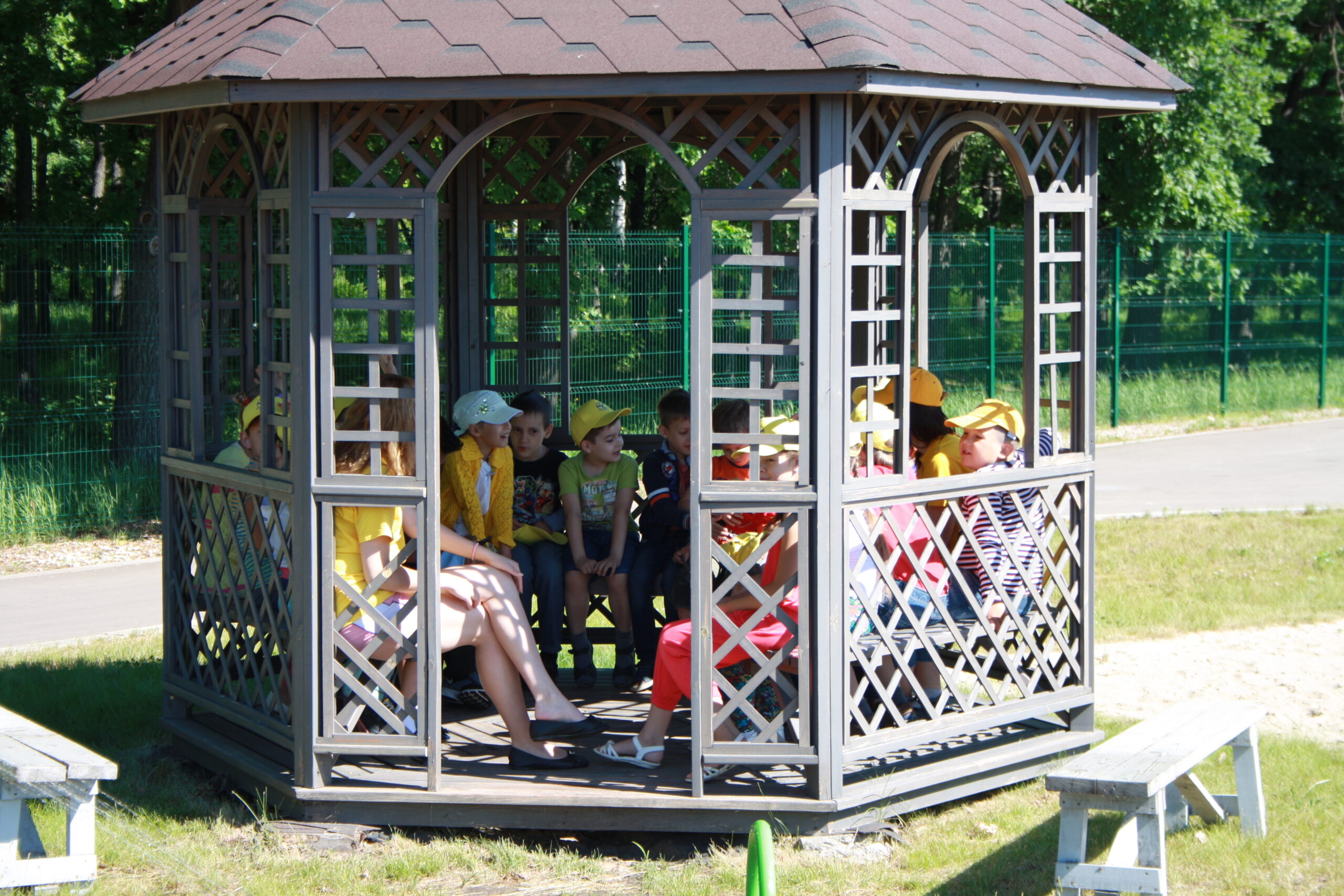 Children wearing hats relaxing and chatting in a wooden gazebo at the camp