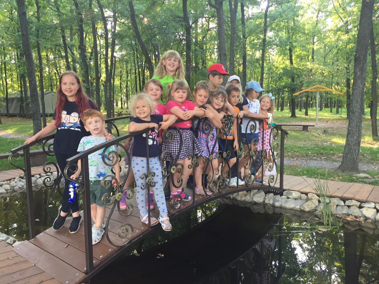 Children happily standing on a small bridge in a green outdoor camp