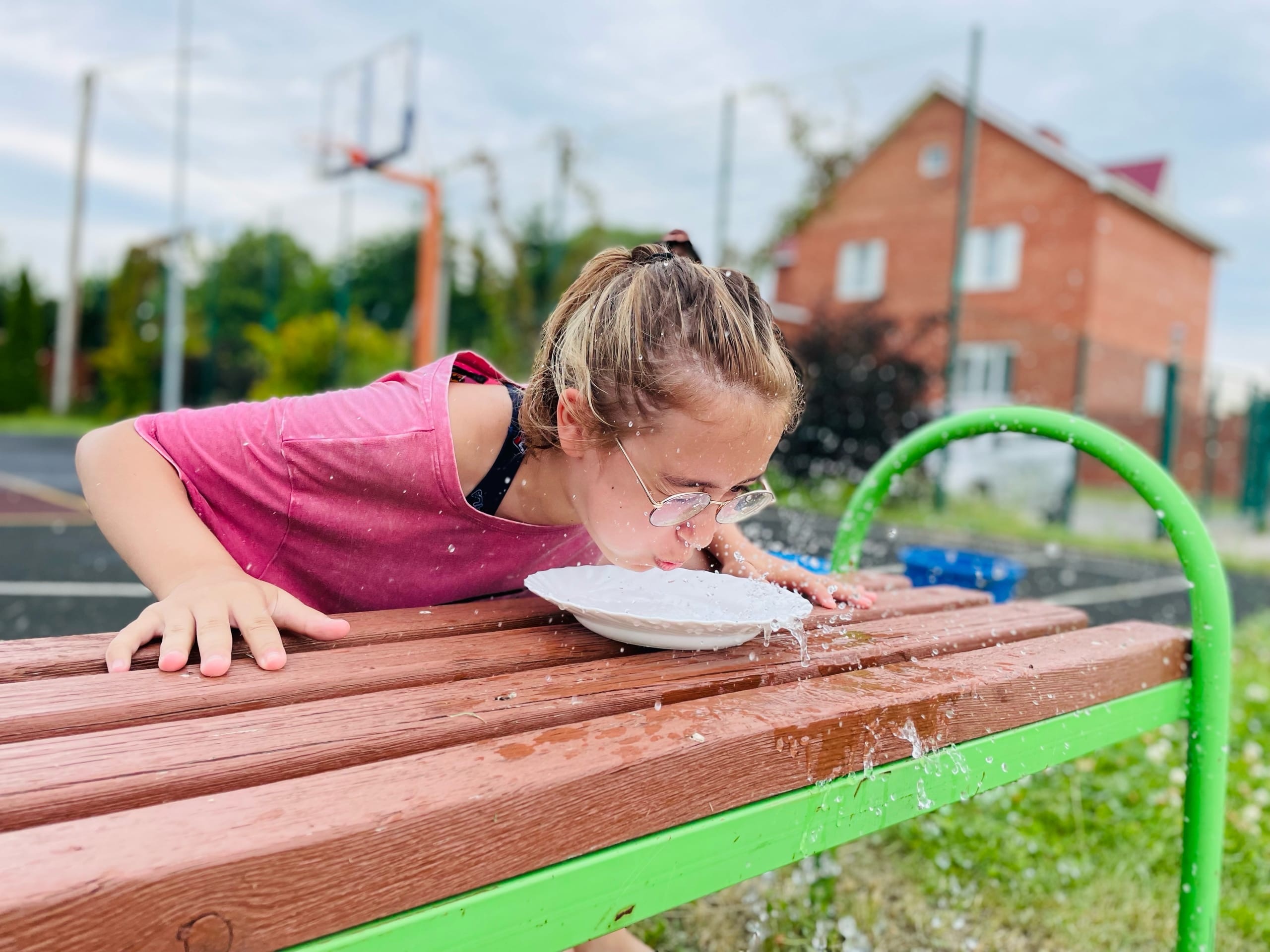 A girl happily drinks water from a fountain outdoors at summer camp