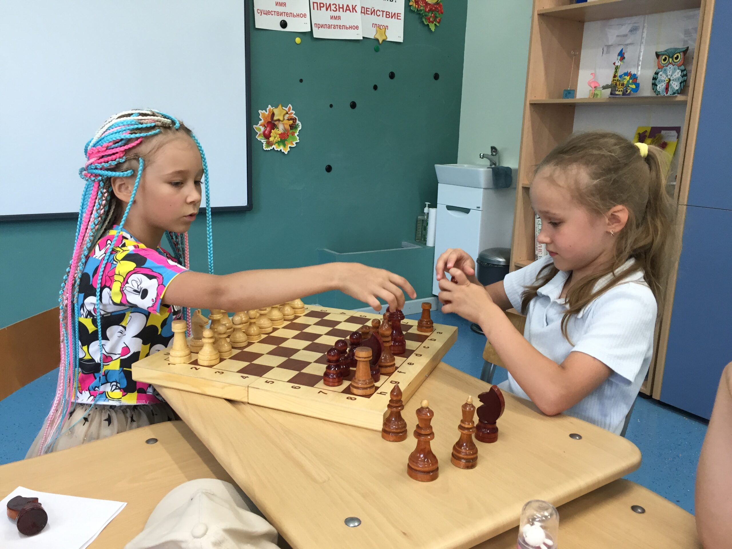 Two girls playing chess carefully at a school desk