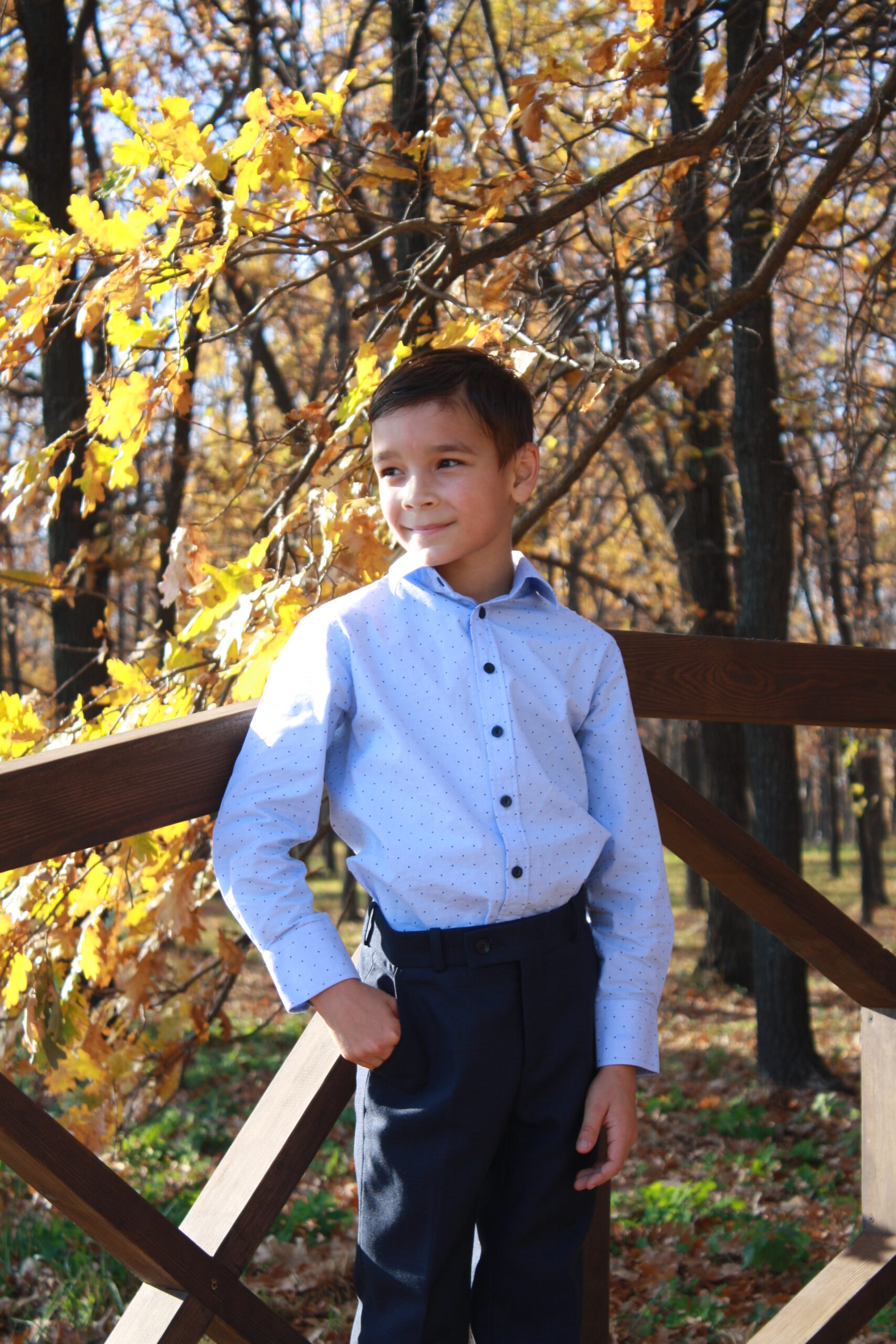 Boy in blue shirt standing against autumn forest background