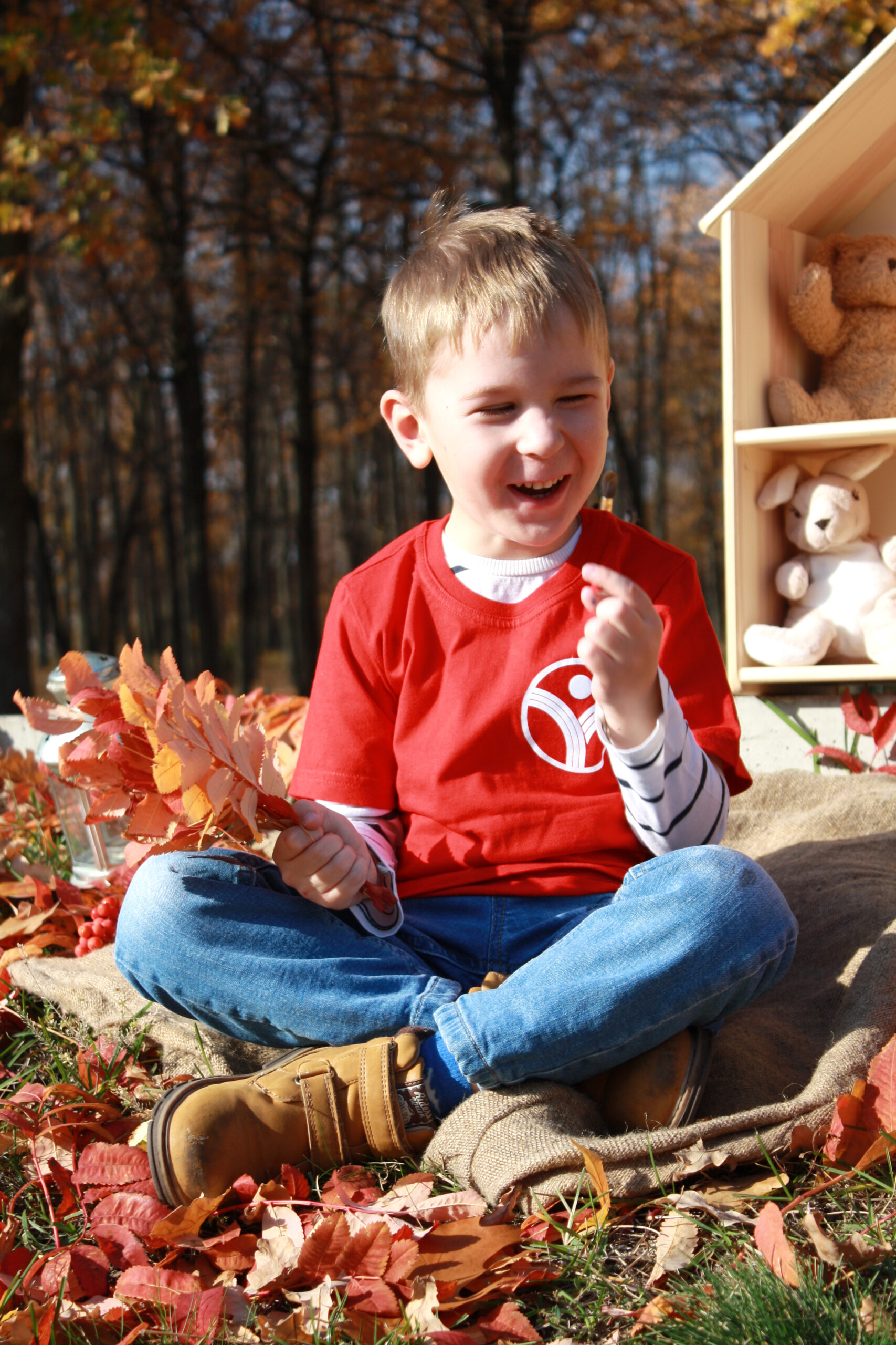 Happy boy in red t-shirt playing with autumn leaves outdoors