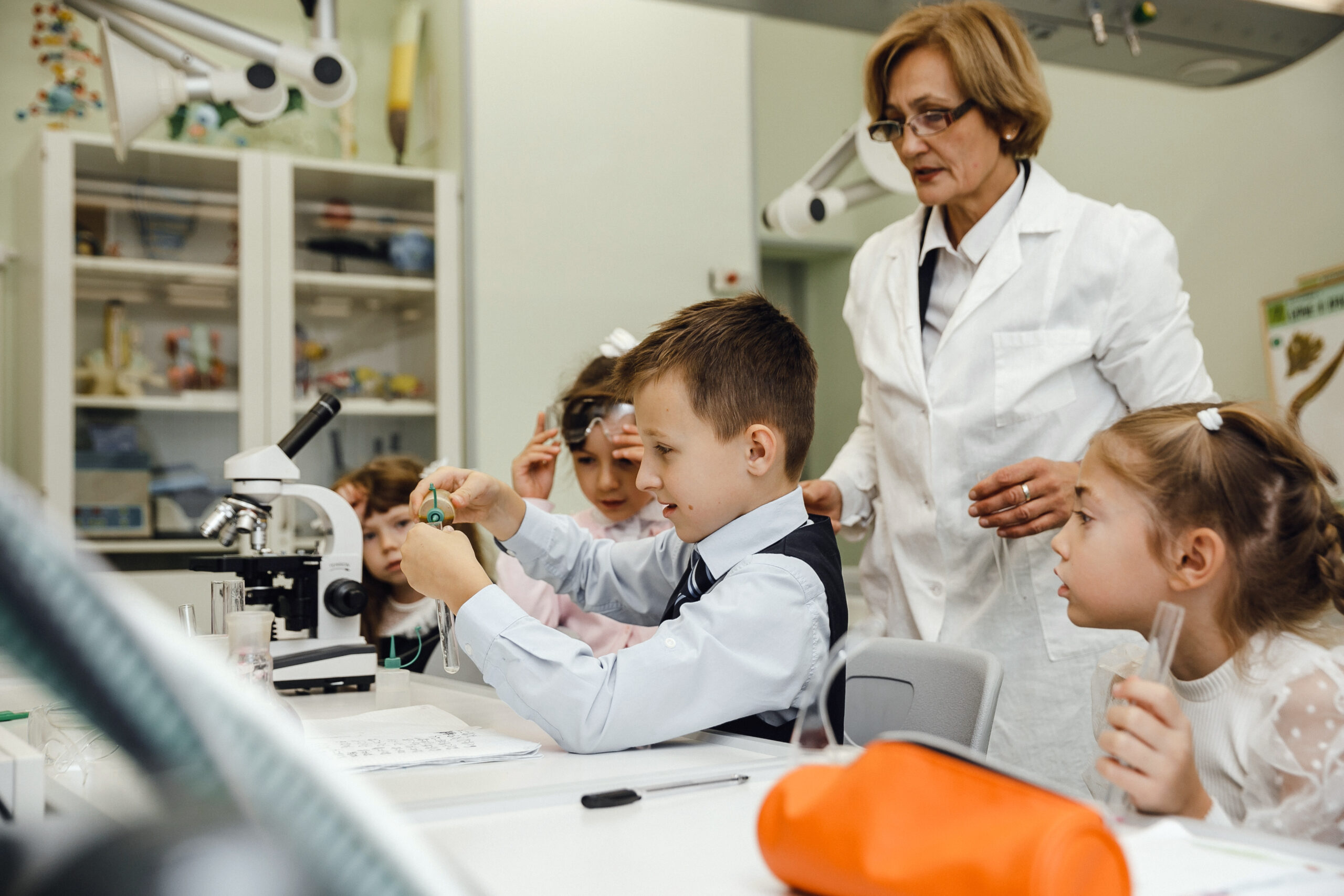 Student with teacher studying objects in test tubes during biology lesson
