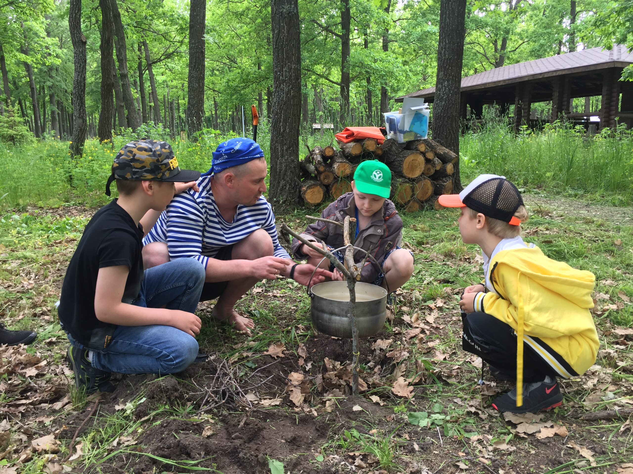 A camp counselor teaches children how to cook over a campfire in the forest