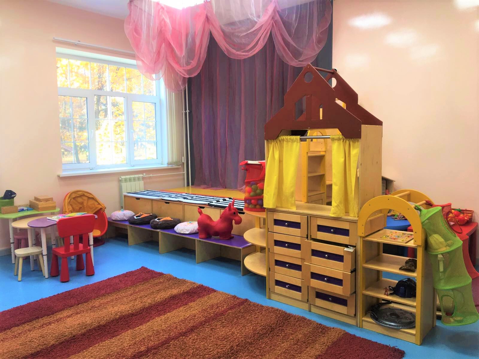 Яркий игровой уголок с мягкими игрушками и мебелью в детской комнате